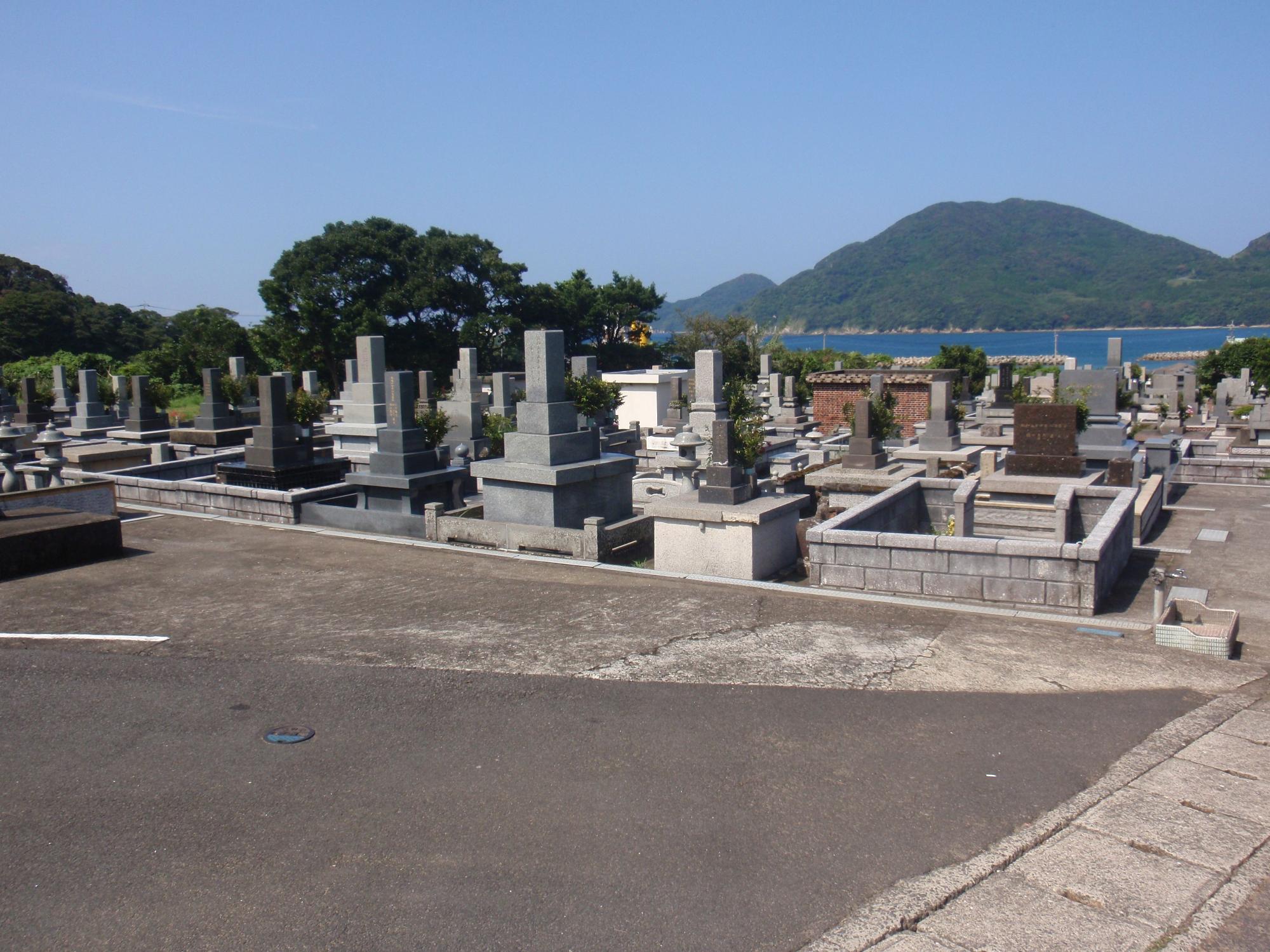 青空の下で整然と並ぶお墓の奥に海を挟んで緑の山が写っている写真