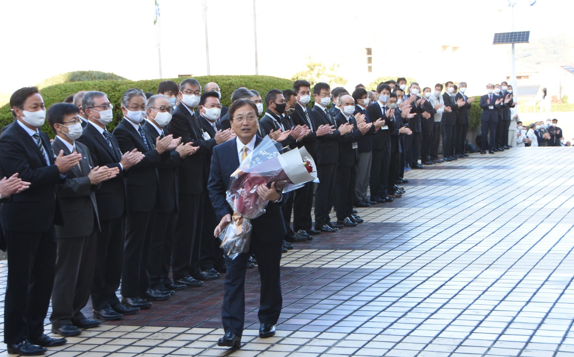 花束を抱え大勢に見守られながら初登庁する田中市長の写真