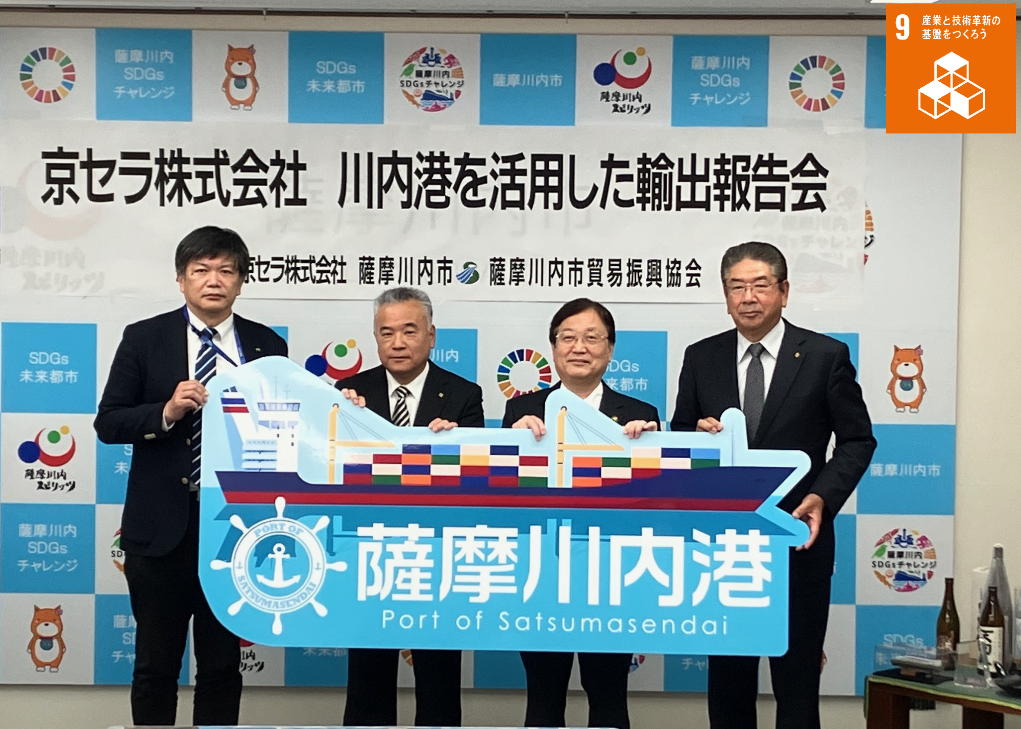 京セラ株式会社鹿児島川内工場長らと川内港のパネルを持ち写真に写る田中市長