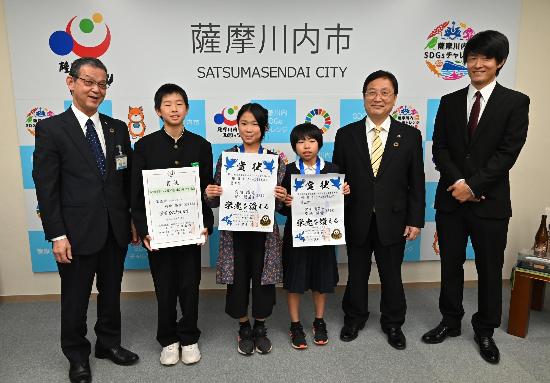 川内ジュニアバドミントンクラブの選手らと並んで写真に写る田中市長・藤田教育長の写真