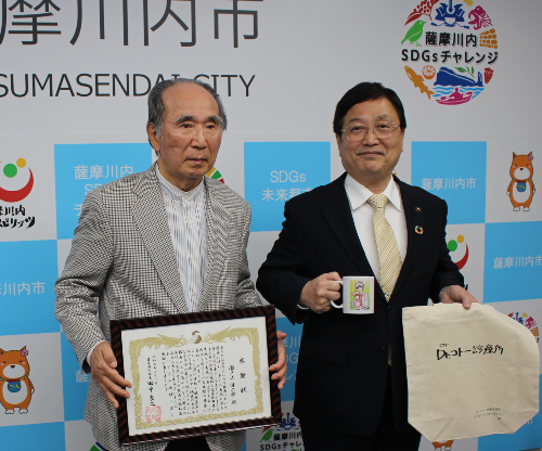 感謝状を手にする瀬戸上先生と並んで写真に写る田中市長の写真