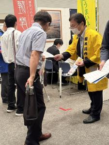 特設ブースでチラシを配りPRを行う田中市長の写真