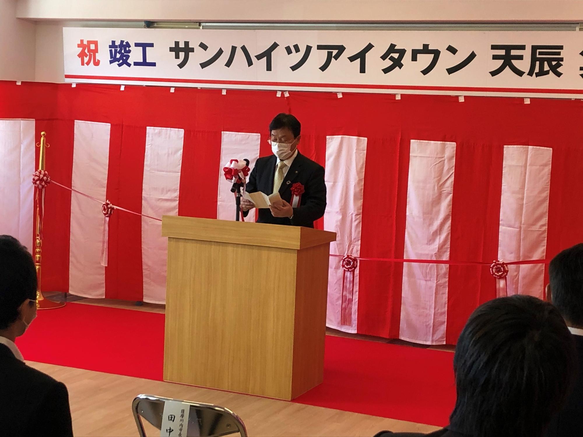 紅白の幕の前で祝辞を述べている市長の写真