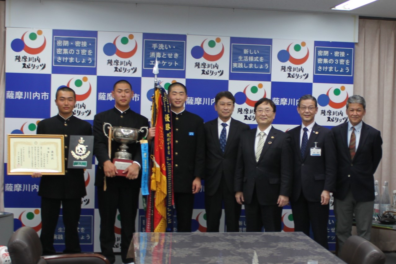 表彰状、盾、トロフィー、優勝旗を手に選手たちが市長らと並んで写真に写っている様子