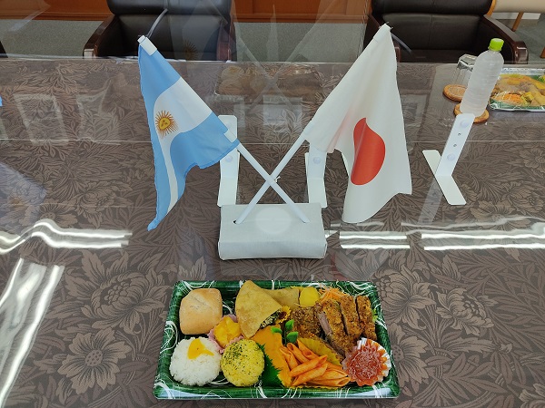 テーブルの上に交差する形で置かれた日本とアルゼンチンの国旗とアルゼンチン料理の写真