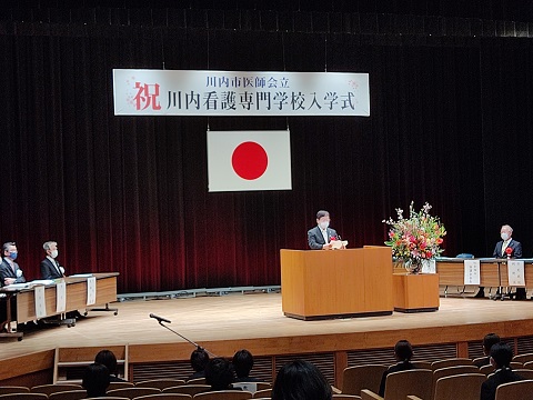 祝川内看護専門学校入学式と書かれた幕と日の丸のもと、壇上で祝辞を述べている市長の写真