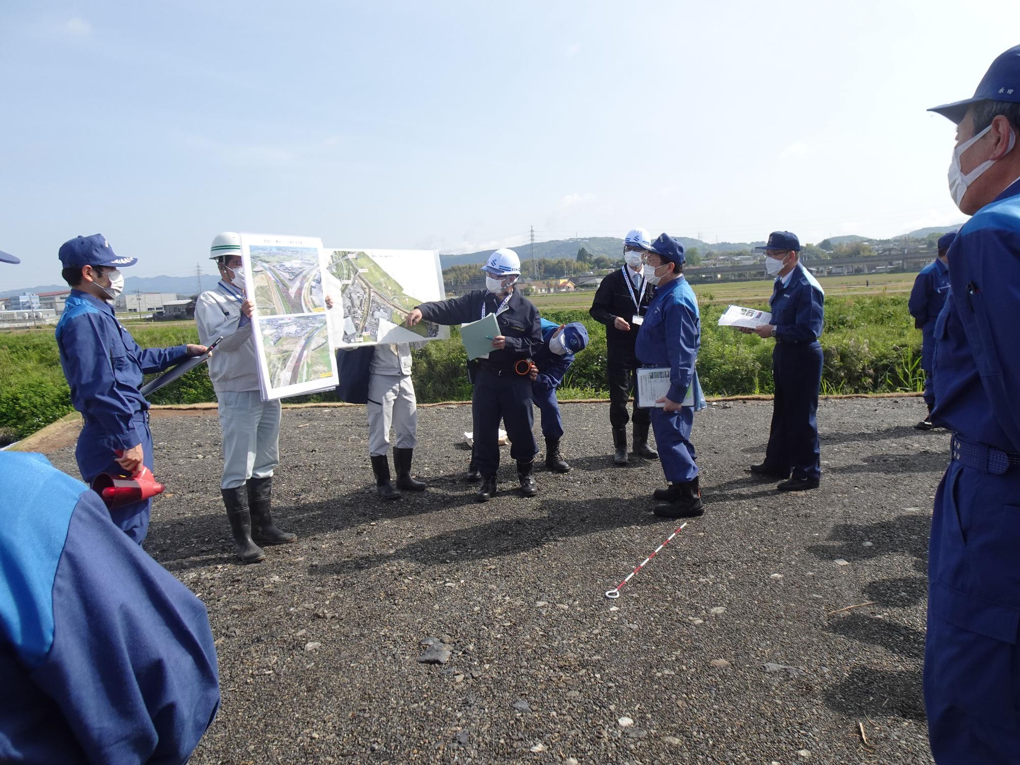スタッフが持っている勝目川と百次川の合流点の写真を、指し棒を使って説明しているスタッフと、その話を聞いている市長の写真