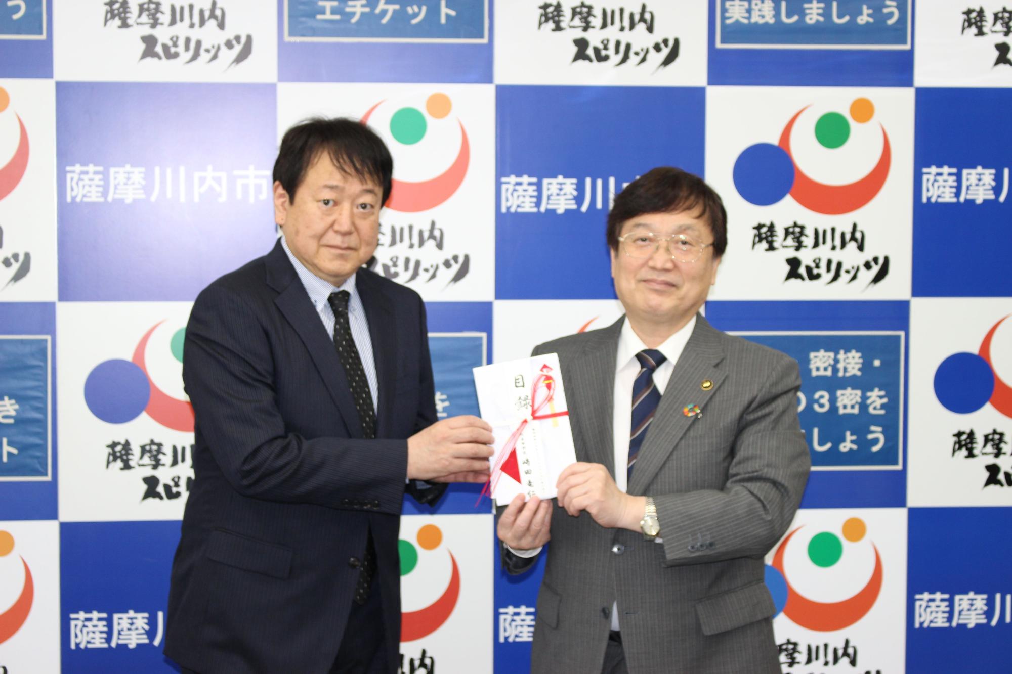 CARESソリューションセンターの代表取締役から寄付金の目録を受け取っている市長の写真