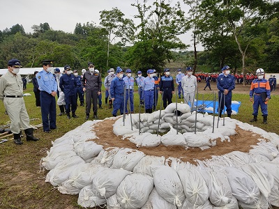 円形に積み上げられた土のうとそれを見ている市長ら防災関係者たちの写真