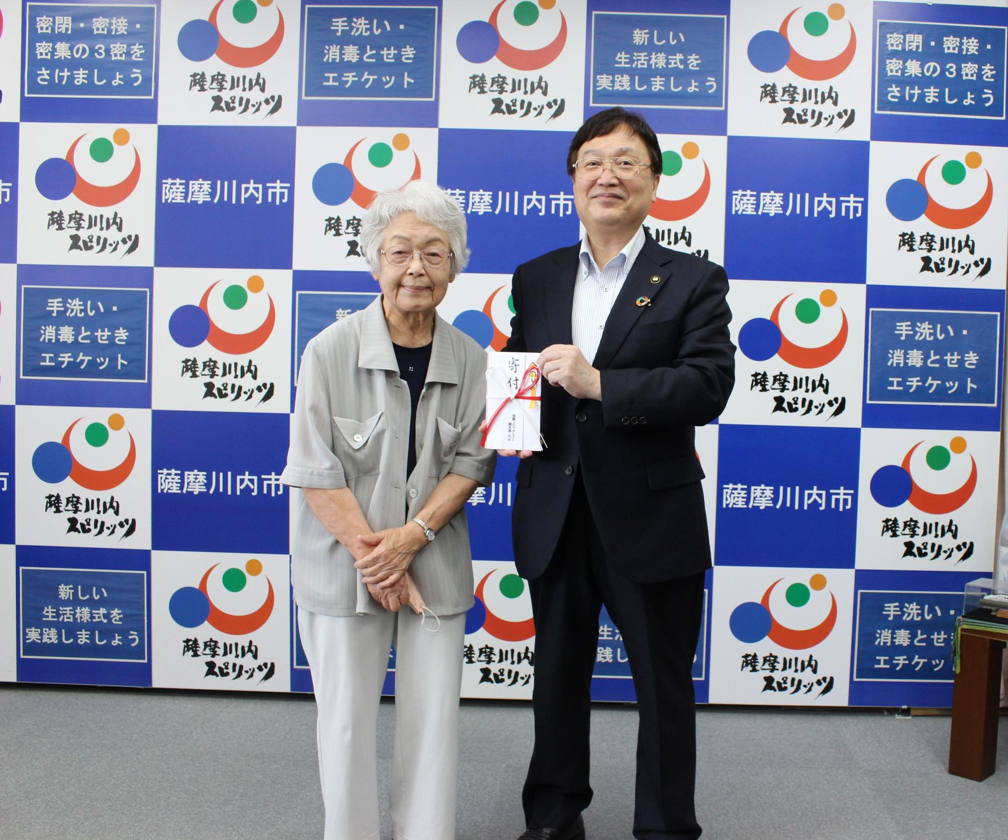 寄付と書かれたのし袋を持つ田中市長とその隣に立つ川内様の写真