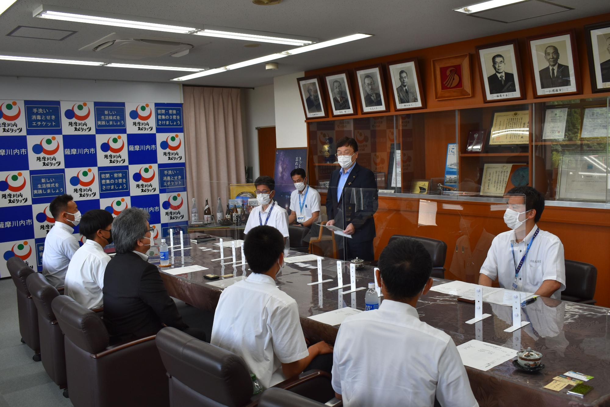 田中市長、スーツ姿の男性たちとテーブルの向かいに座る学生たちの写真