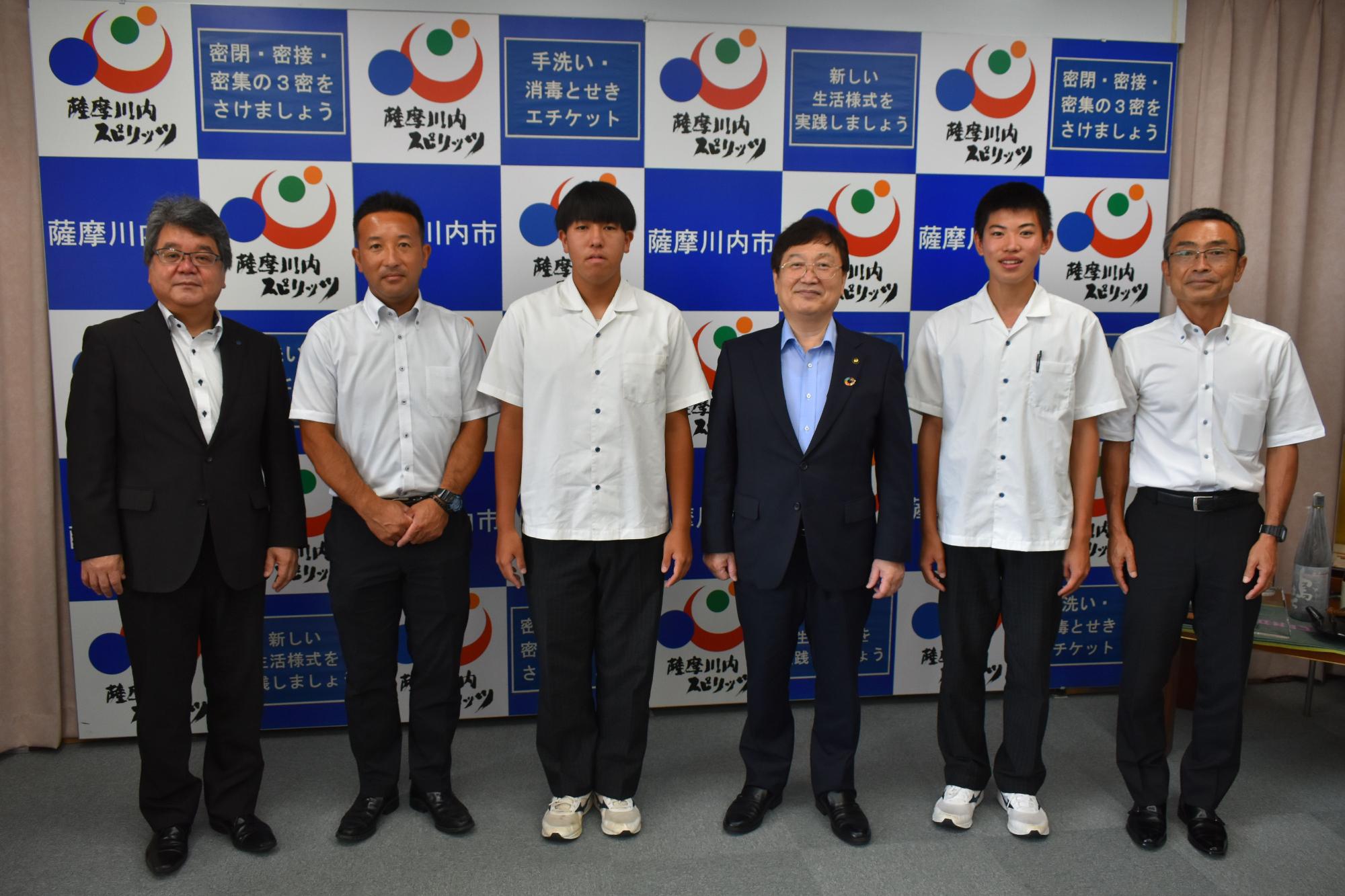 田中市長、スーツ姿の男性たちと並んでいる高校生たちの写真