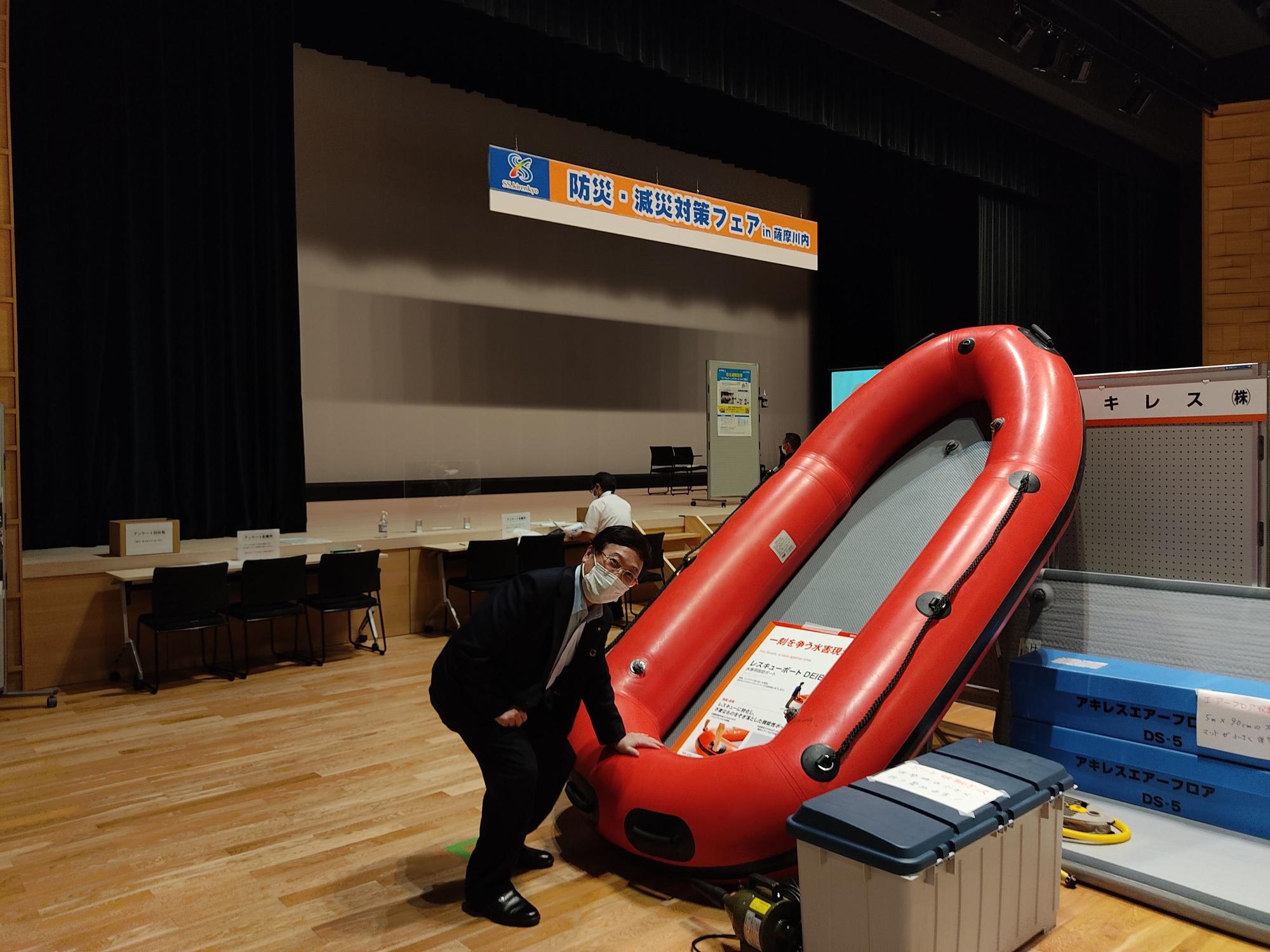 立てかけられたゴムボートに手を添えるスーツ姿の男性