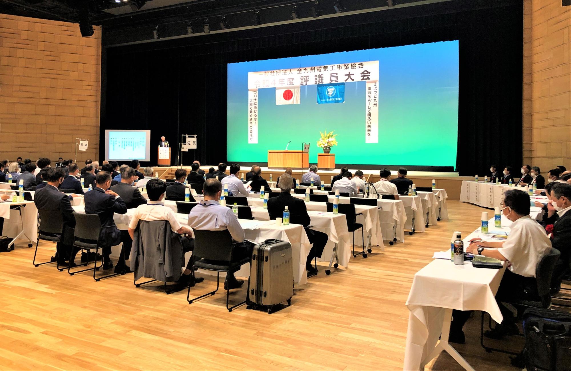会場内で席についている大勢のスーツ姿の男性たちの写真
