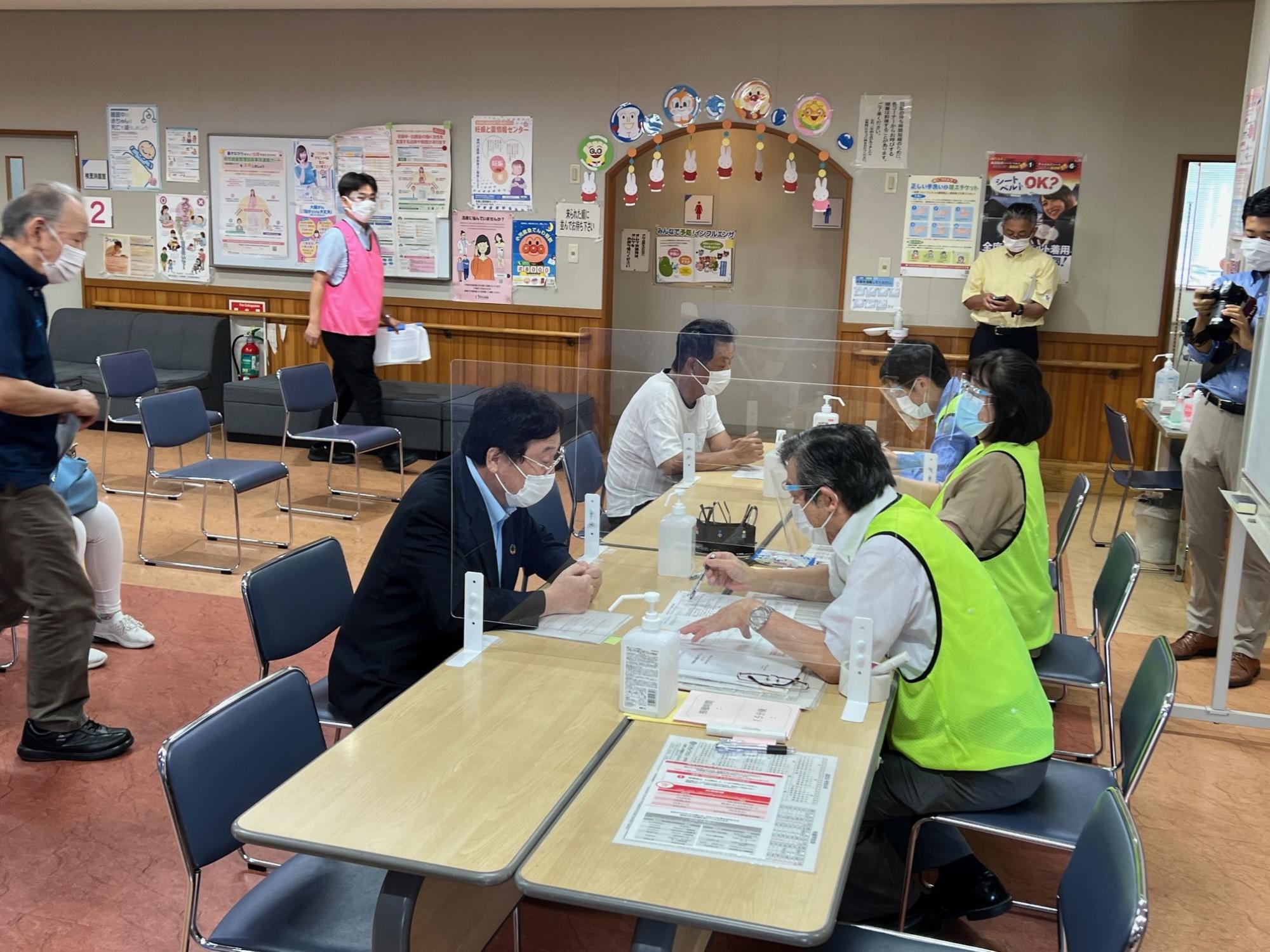 黄緑のビブスを着た男性とテーブル上の紙を見ながら話すスーツ姿の男性の写真