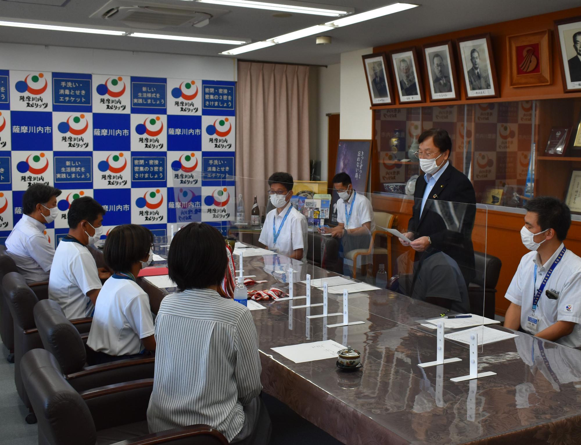 スーツ姿の男性たちとその向かいに座る小学生たちの写真