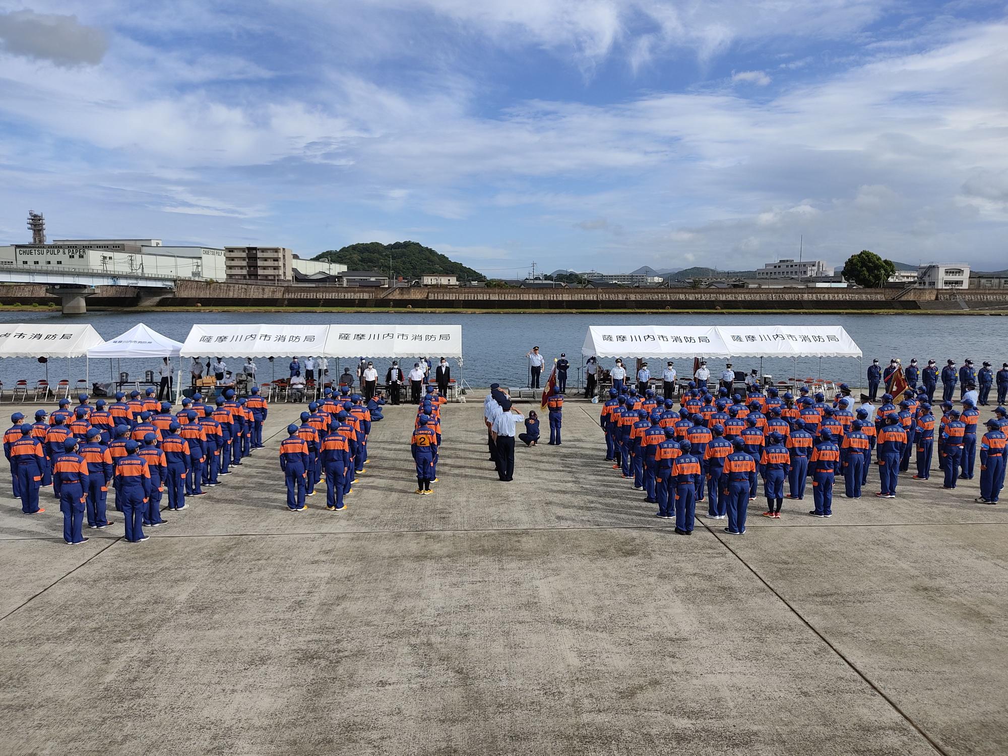 川の前で整列する大勢の消防団員たちの写真