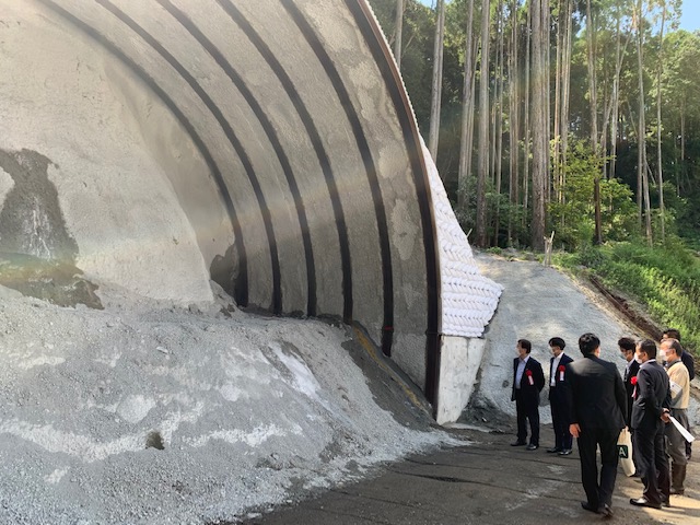 建設途中のトンネルの前にいるスーツ姿の男性たちの写真