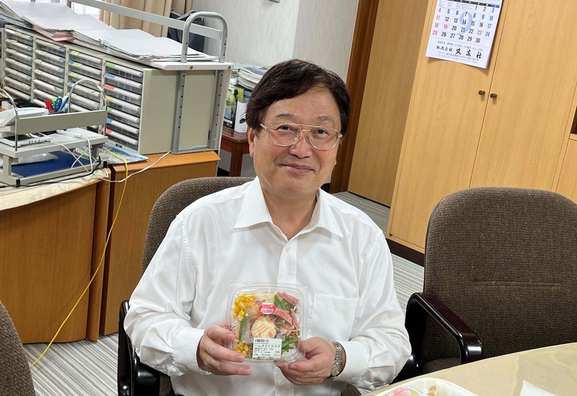 サラダを手に持って笑う田中市長の写真