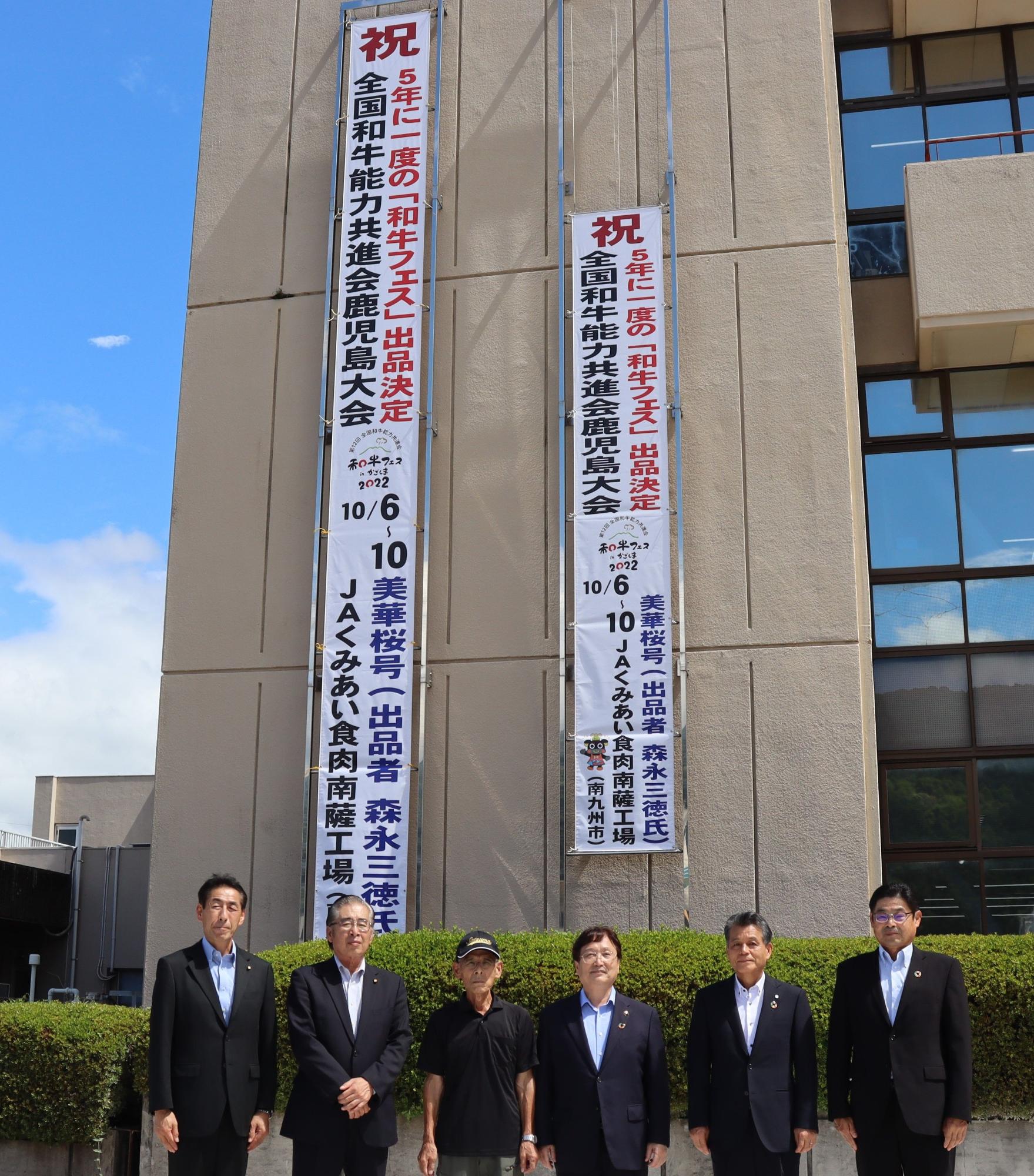 本庁舎に下がった全国和牛能力共進会鹿児島大会の垂れ幕とその前に並んでいるスーツ姿の男性たちの写真