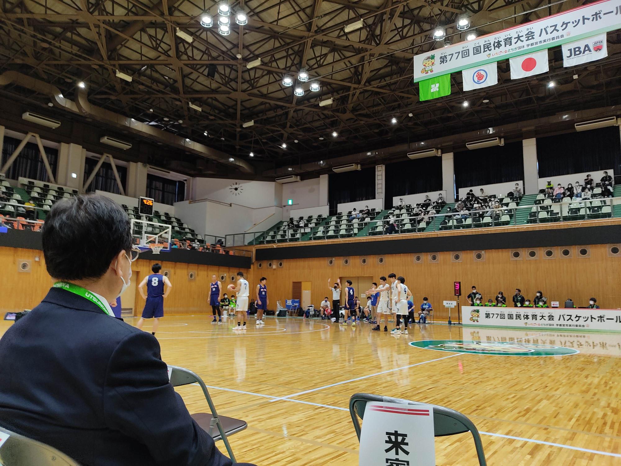 男子バスケの試合を観戦するスーツ姿の男性の写真