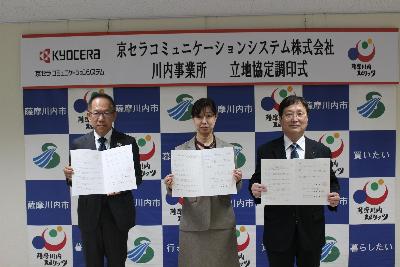 調印れた立地協定書を開いている市長と鹿児島県北薩地域振興局長と京セラコミュニケーションシステムの関係者の写真