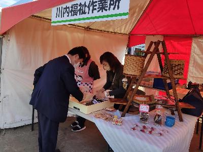 出展者の商品と手に取る田中市長の写真