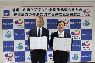 署名した協定書を手に並んで写真に写るアクサ生命鹿児島支社長と田中市長の写真