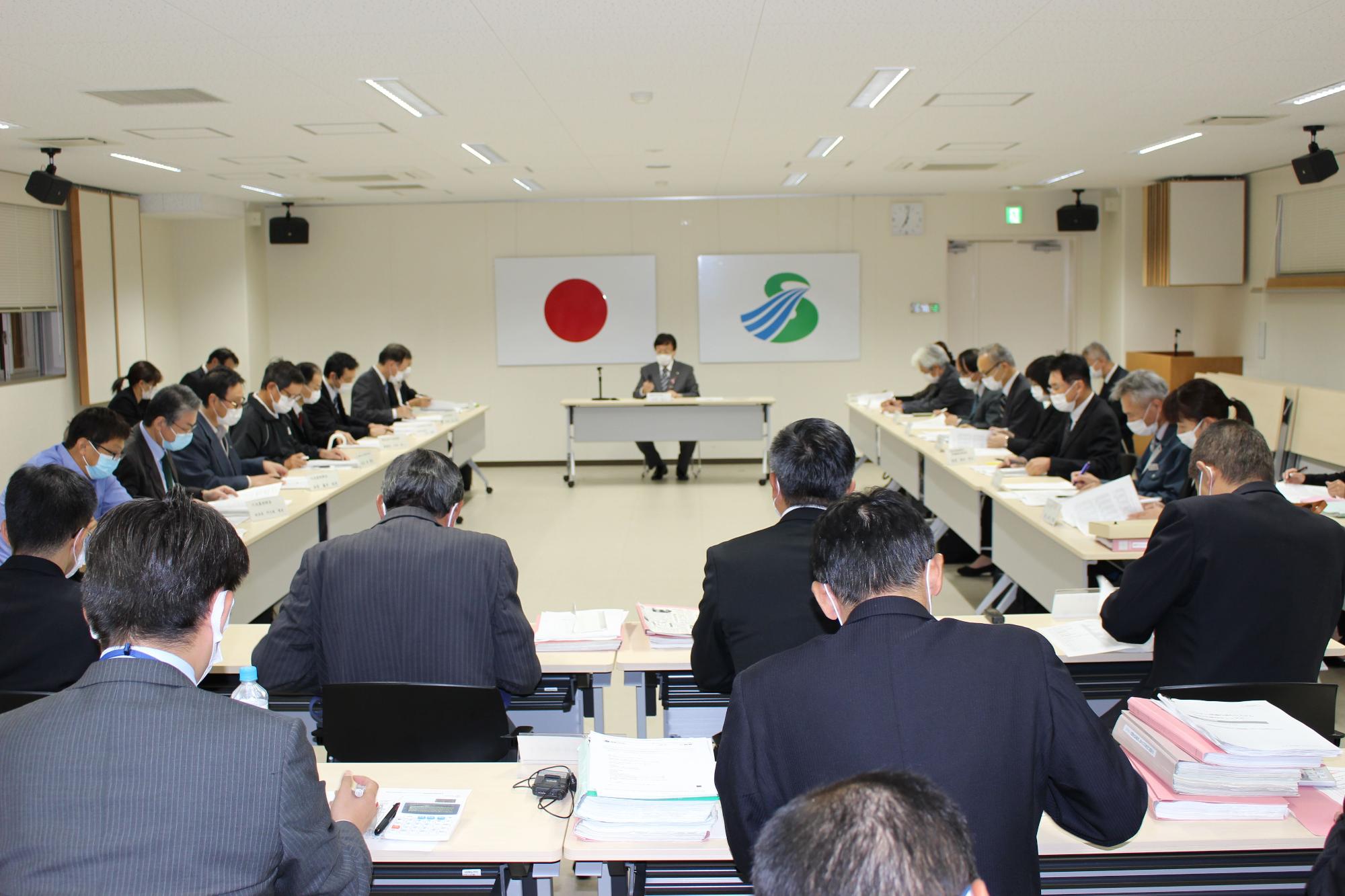 会議室で机に並べられた資料を見ながらスーツ姿の男女が会議を行っている様子の写真