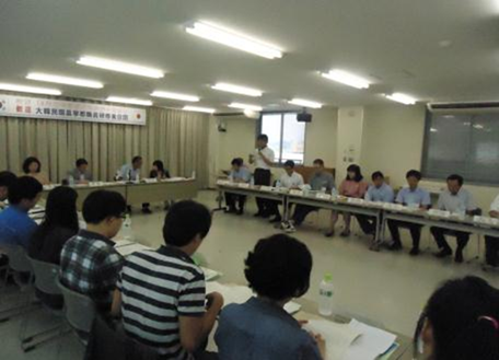 室内に並べられた机に座り資料を広げている男女たちの写真