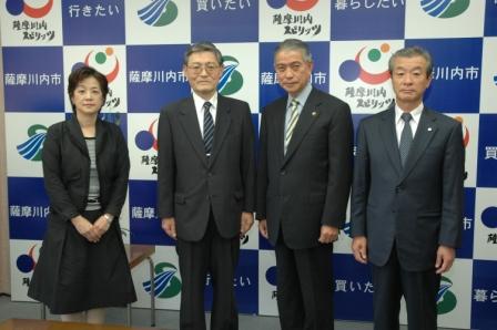 「行きたい」「暮らしたい」「薩摩川内市」と書かれたパネルの前で、スーツ姿の男性3人と、スーツ姿の女性1人が横一列に並んだ記念写真