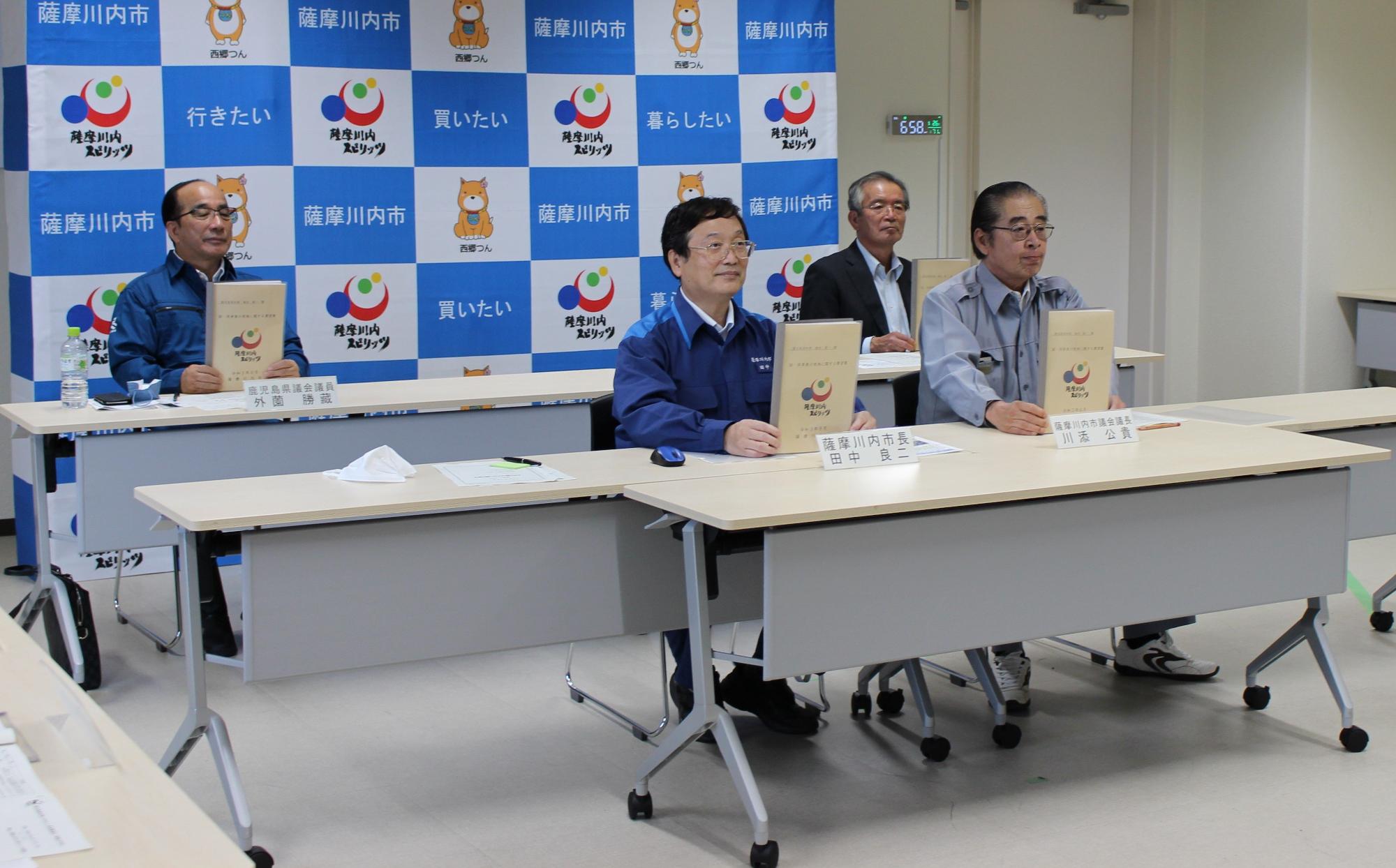薩摩川内スピリッツと書かれた本を掲げる田中市長たちの写真
