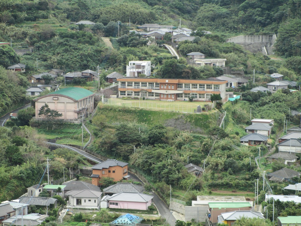 古い小学校校舎と、斜面に並んでいる集落の写真
