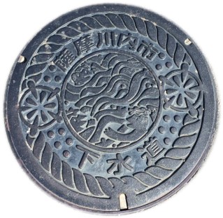 真ん中の丸部分で河童が泳ぎ丸部分を大繩で囲んだ内側の隙間に花火が上がっている川内のマンホール蓋の写真
