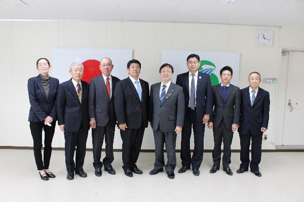 スーツを着た男性7名女性1名が日本国旗と薩摩川内市市章を背景に一列に並んで正面を向いている写真
