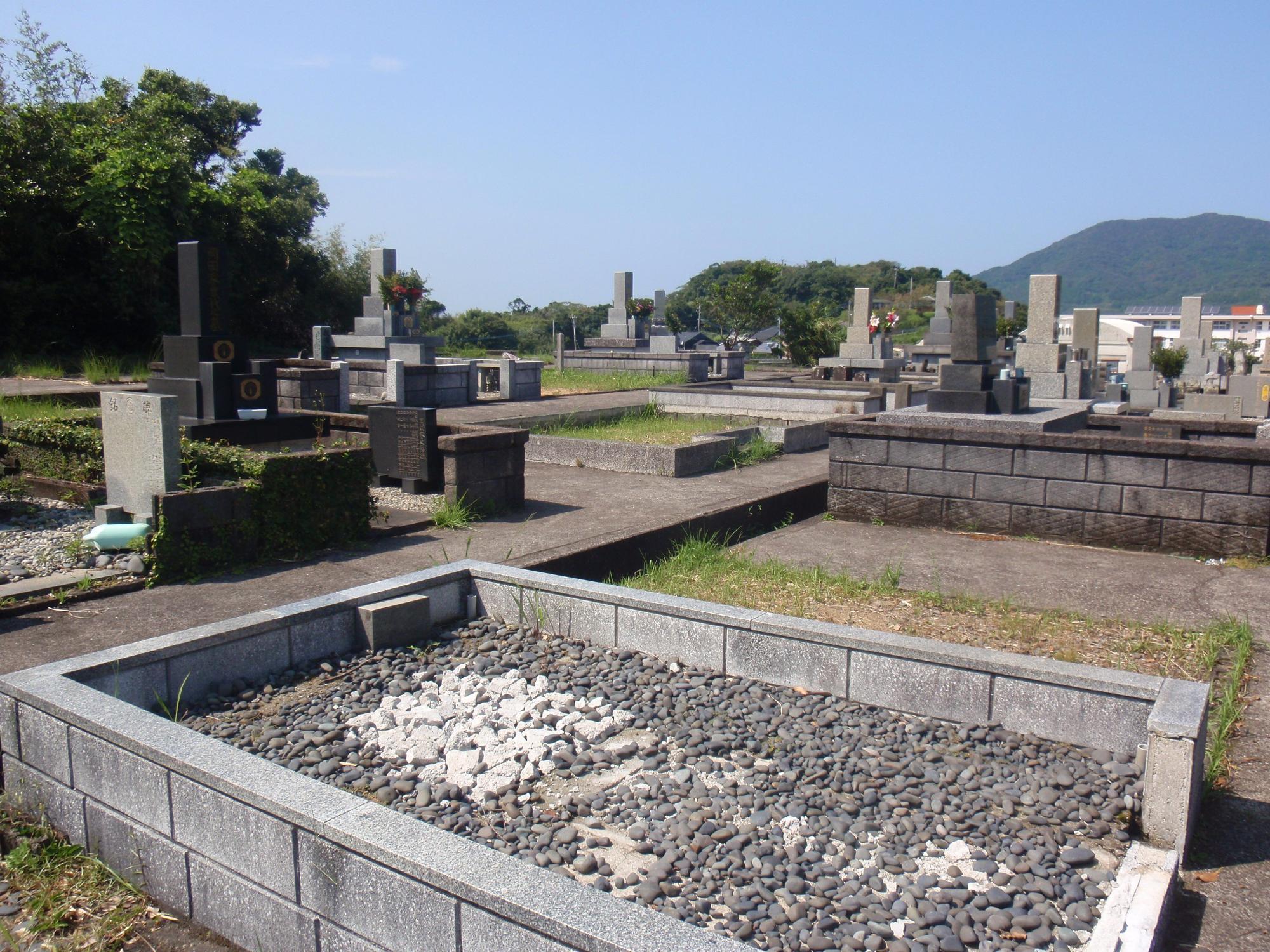 青空の下で四角く区切られた墓石のない空き区画と、奥に建つ数基のお墓の写真
