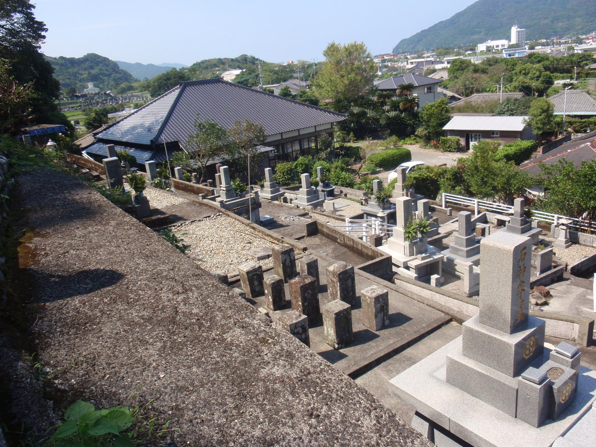 青空の下、お墓が点在するいくつもの段になった墓地の奥に町が広がっている景色の写真