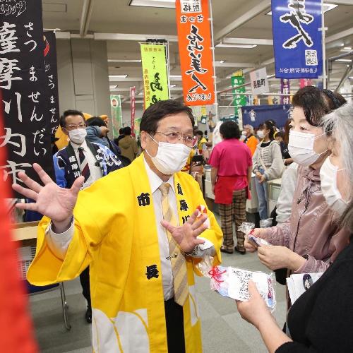 来場者へノベルティを配布し市のPRをする田中市長の写真