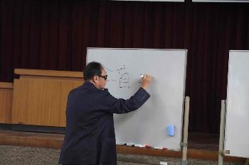 ホワイトボードに文字を書く松永信也氏のようす