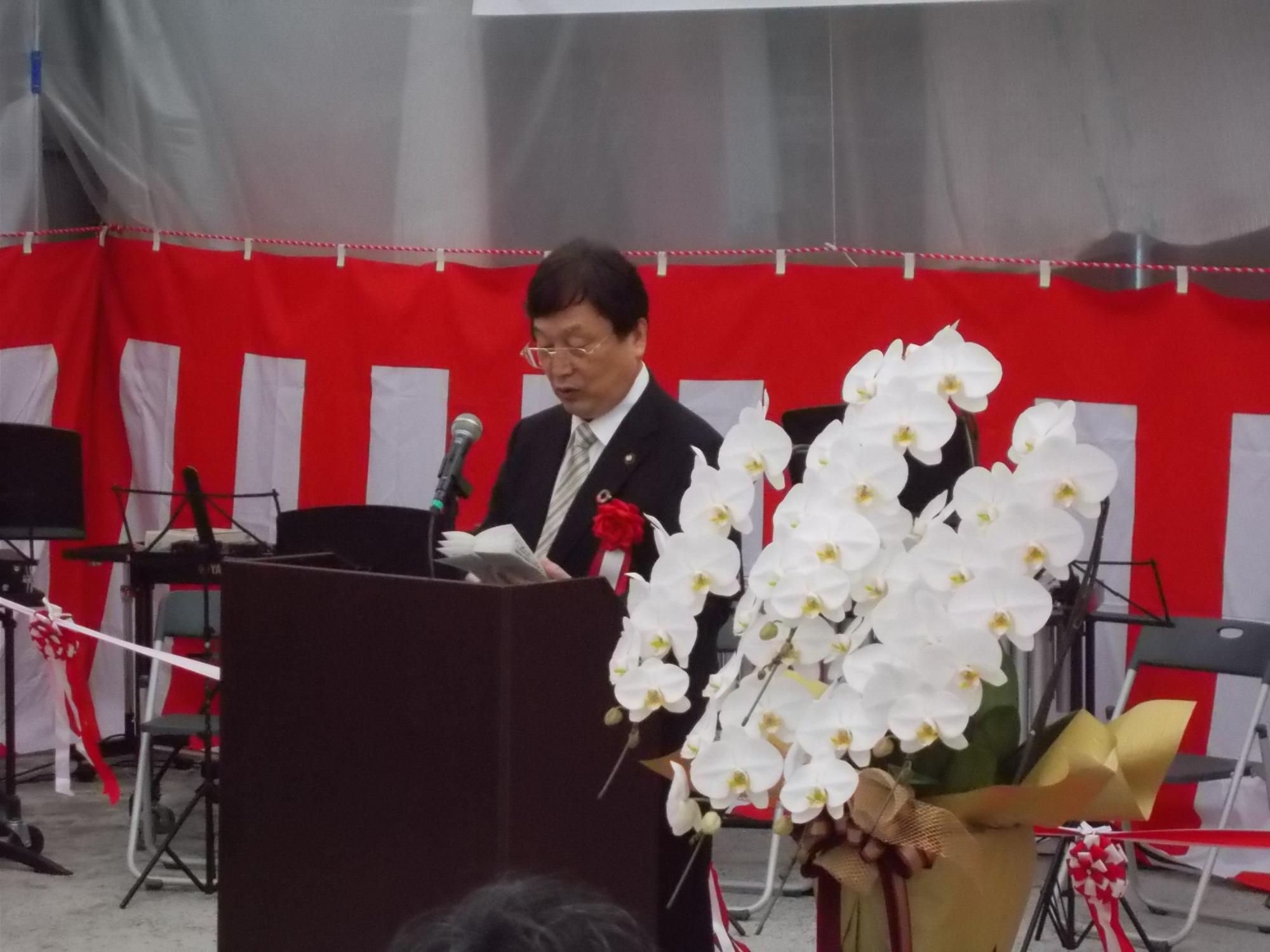 白い胡蝶蘭の横でスピーチする田中市長の写真