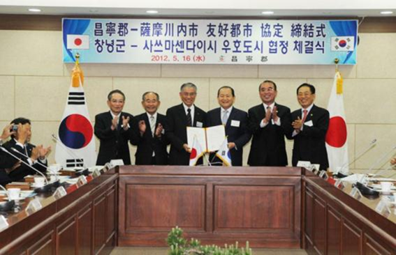 日本と韓国の国旗の間で横に並ぶスーツ姿の男性たちの写真