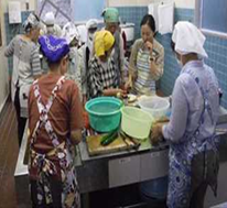 エプロンを着けた女性たちが青いタイル張りのキッチンで料理をしている写真