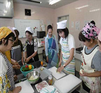 エプロンとバンダナを着用した女性たちが料理をしている写真
