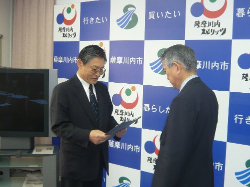 書面を手に持った男性が、向かい合って立つ男性に内容を読み上げている様子の写真