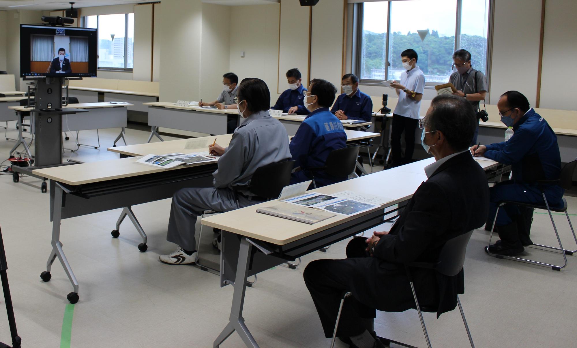 会議室でモニターに映っている鹿児島県知事と、メモを取るなどして話を聞く薩摩川内市職員の方々の写真