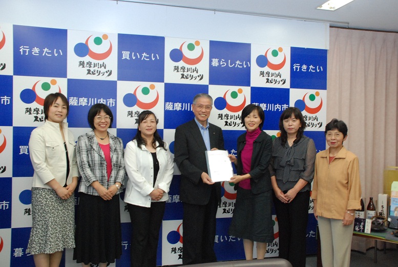第4期薩摩川内市女性50人委員会のメンバー6名が、生活者の視点で練り上げた全25項目の提言書を市長に提出している様子の写真。