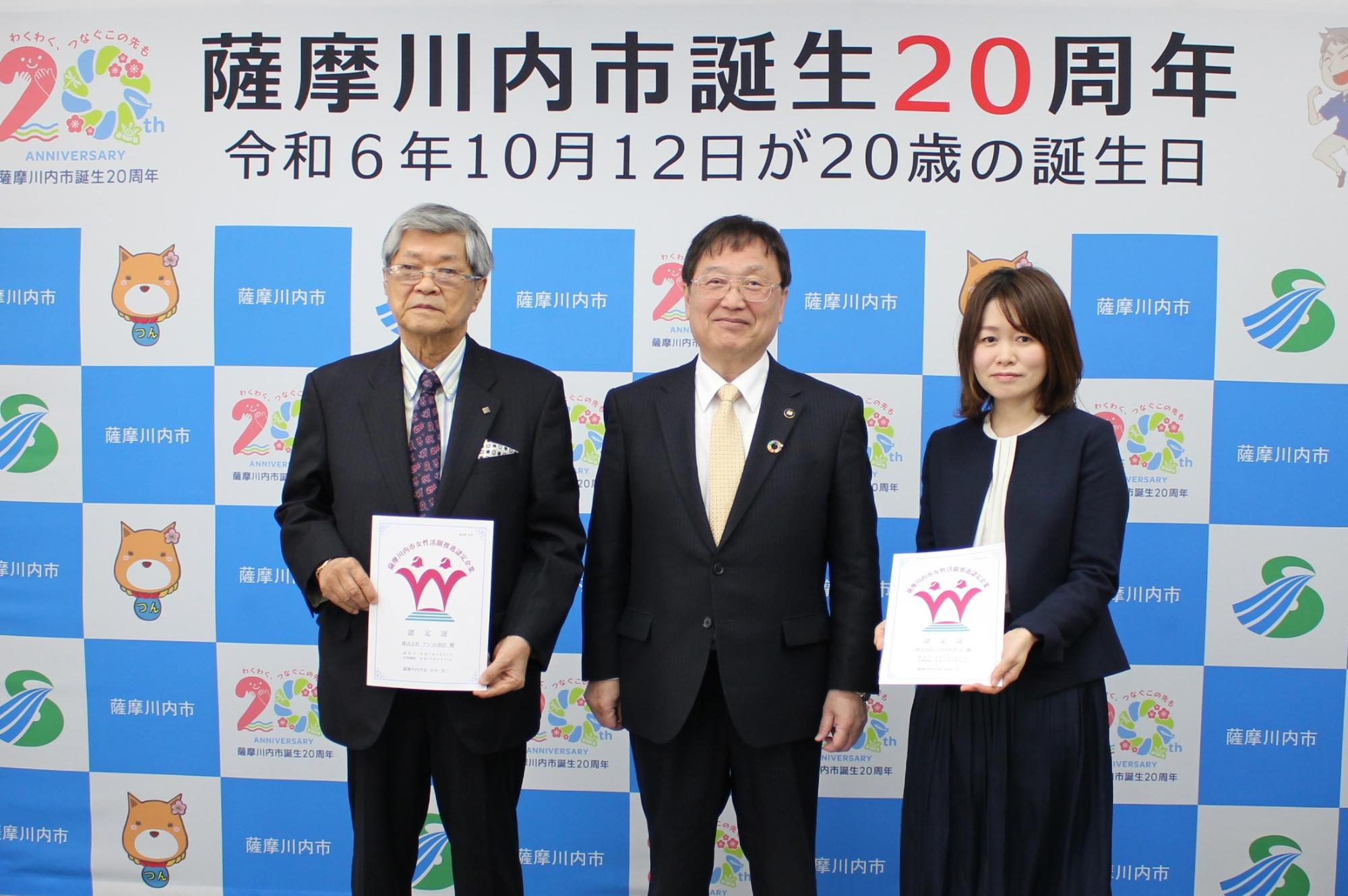 認定証を手にもって正面を向いている株式会社アシスト設計、代表取締役社長の今村裕氏と株式会社ハウスサポート、専務取締役の今村裕子氏と田中市長