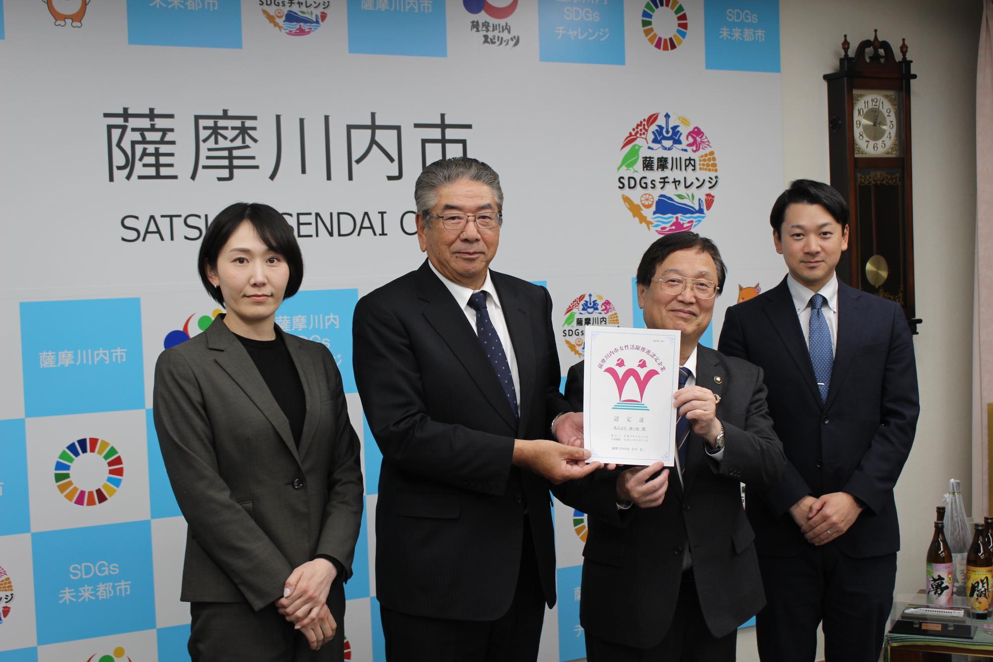 認定証を持っていいる4人の集合写真(左から株式会社橋口組企画部主任山口なつみ氏、株式会社橋口組専務取締役橋口宗一朗氏、薩摩川内市長、株式会社橋口組代表取締役橋口知章氏）