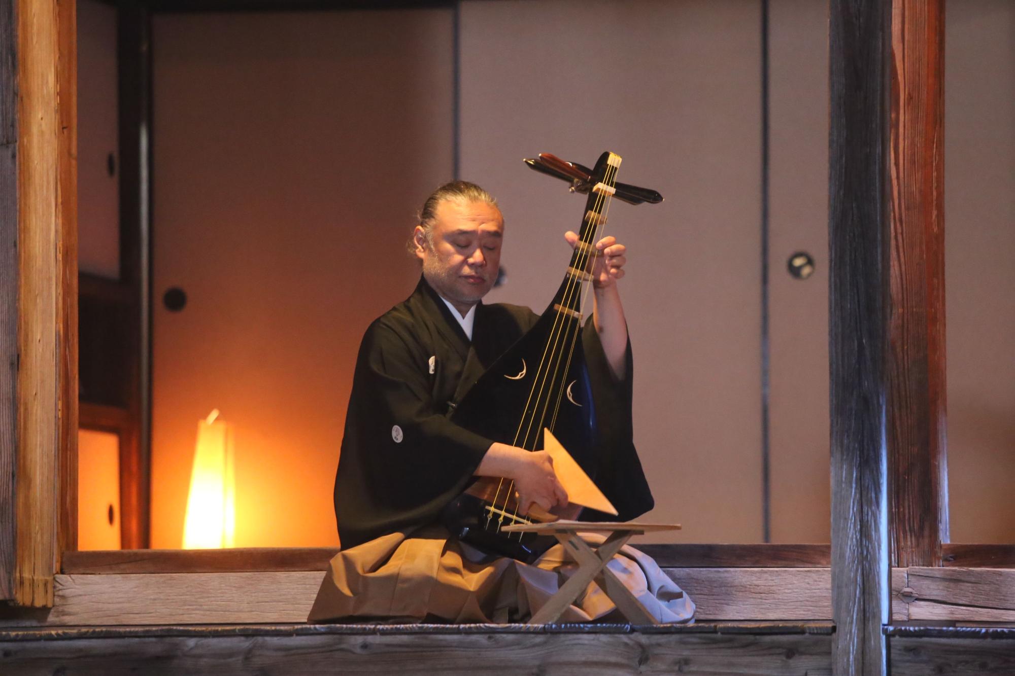 和風の邸宅の中で座りながら和楽器を演奏する着物姿の男性の写真